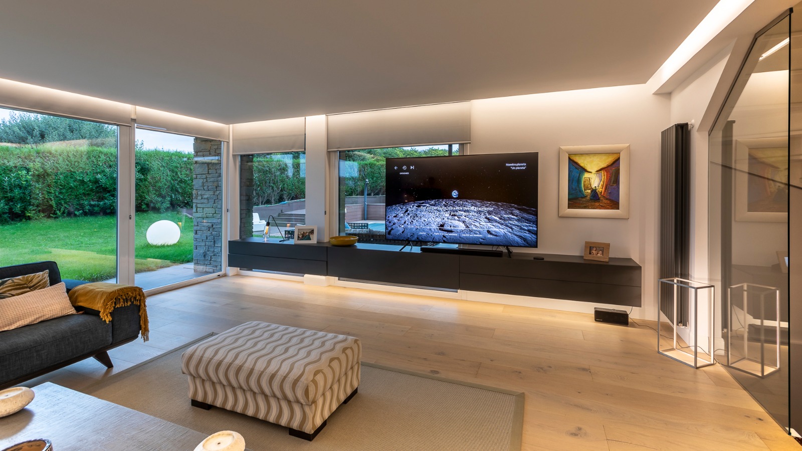 Salón de una vivienda en Sopelana diseñada por Andoni Bollada, con mueble de televisión suspendido y ventanales al jardín