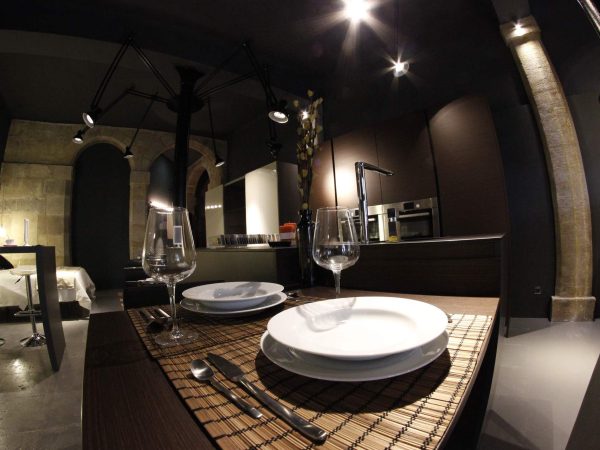 Mesa puesta con copas y platos blancos en un espacio con muros de piedra y techo oscuro